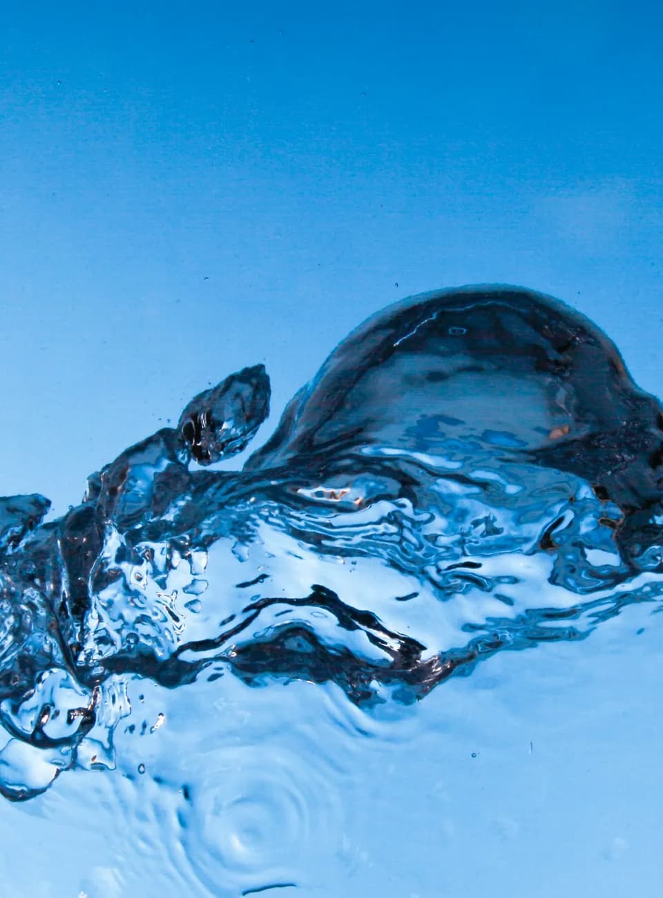 Clear water breaking into a wave against a bright blue field